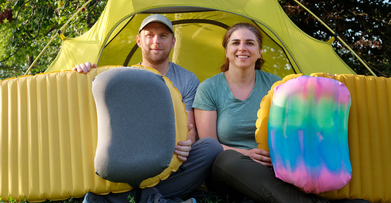 Brian and Rita Founders of Pillow Strap holding two Pillow Straps on two sleeping pads sitting in a tent 